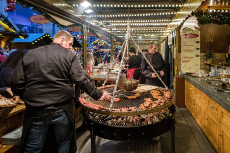 Foto de Bonn, Alemania - 16 de diciembre de 2023: Vista de un puesto de comida con una barbacoa gigante que vende varias salchichas y filetes alemanes en el Mercado de Navidad en Bonn Alemania - Imagen libre de derechos