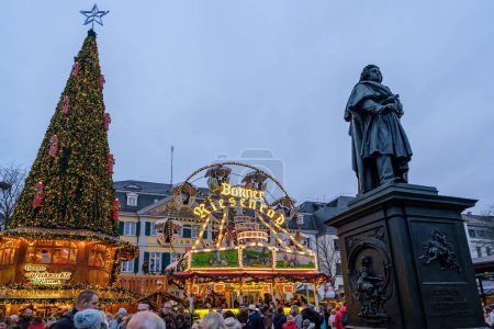 Foto de Bonn, Alemania - 16 de diciembre de 2023: Vista de la estatua de Beethoven, un árbol de Navidad iluminado y una noria en el mercado de Navidad de Bonn Alemania - Imagen libre de derechos