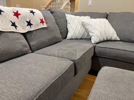 Photo for Close up, selective focus on an L shaped gray couch with white pillows and a star covered blanket in a bright living room - Royalty Free Image