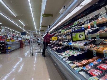 Photo for Everett, WA USA - circa December 2022: Wide view of a grocery store employee restocking the refrigerated meat department. - Royalty Free Image