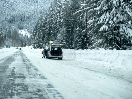 Foto de Stevens Pass, WA USA - circa December 2022: Wide view of vehicles putting on snow tire chains on the side of the road during snowy conditions. - Imagen libre de derechos