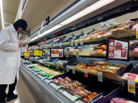 Foto de Everett, WA USA - circa Diciembre 2022: Amplia vista de un empleado de una tienda de comestibles reponiendo el departamento de carne refrigerada. - Imagen libre de derechos