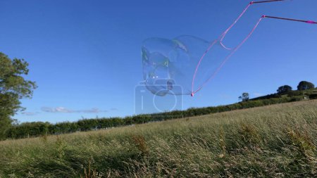 Foto de Burbuja de jabón gigante con una varita de burbuja en un campo en verano - Imagen libre de derechos