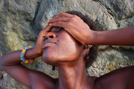 Sereno disparo en la cabeza de una mujer africana abrazando su belleza afro contra el relajante telón de fondo de rocas