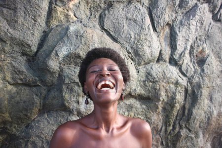 Strahlender Kopfschuss einer afrikanischen Frau, ihr Afro und ihre Ohrringe, die ihr reiches kulturelles Erbe an den Felsen widerspiegeln