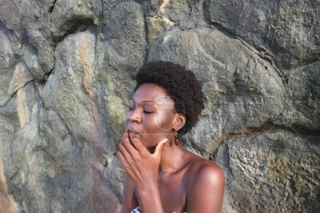 Captivating head-shot of an African woman, her afro and earrings harmonizing with the rocky backdrop