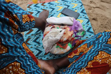 Wild colors of fabric legs of a black woman sitting on the beach with bag and phone