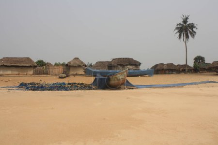 A traditional fishing village with thatched-roof huts and a fishing boat resting on the sandy beach. Nets are laid out to dry under the sun.