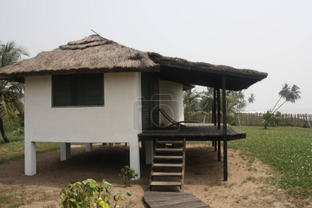 Ein zeitgenössisches Haus auf Stelzen mit Strohdach, gelegen auf einer Grünfläche in Strandnähe.