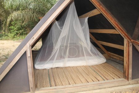 A cozy tent with an open front, revealing a neatly arranged bed with a mosquito net inside, set in a natural outdoor environment.