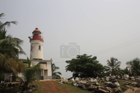 A beautiful lighthouse situated by the beach in Ghana, surrounded by lush greenery and rocks, showcasing the rustic charm of coastal architecture.