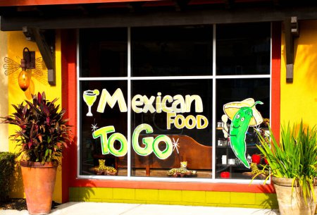 Photo for Mexican food to go hand painted store front sign on glass panes.   Margarita and jalapeno pepper design. Orange, red, yellow, green colors with pretty potted plants out front. November 2, 2023 Florida - Royalty Free Image