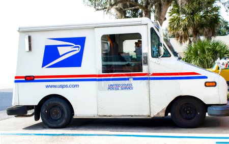 Téléchargez les photos : Ocala, Floride, États-Unis 2 novembre 2023 Camion USPS livrant du courrier dans une rue de banlieue garée dans un espace occupé. couleurs concept blanc et bleu rouge avec emblème de la mascotte de Pygargue à tête blanche américain - en image libre de droit