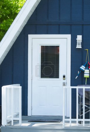 Gros plan de mignon adorable Une maison en forme de triangle cadre ou à la maison avec une couleur bleu profond avec porte blanche, garde-corps porche avant en bois, décor à thème nautique