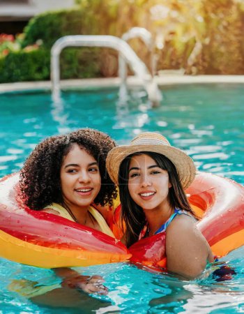 view of two young middle aged  women, relaxing in a pool floatie together in summer time and look at camera with complicity. girlfriends. couple lgbtq concept