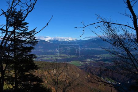 Foto de Cordillera cubierta de nieve en las montañas de Karavanke en Gorenjska, Eslovenia con pueblo, campos y bosque en las llanuras a continuación - Imagen libre de derechos