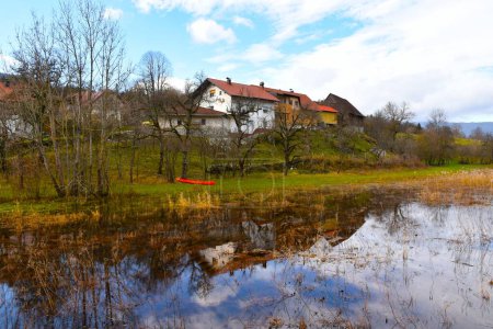 Foto de Pueblo de Laze pri Gorenjem Jezeru y un reflejo de los edificios en el lago Cerknisko jezero en Notranjska, Eslovenia - Imagen libre de derechos