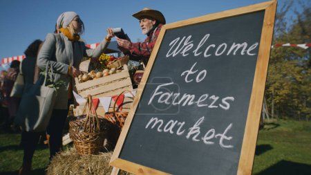 Die Menschen kaufen ein, wählen Obst und Gemüse auf dem örtlichen Bauernmarkt aus, verpacken Waren in Ökotüten. Herbstmarkt am Wochenende im Freien. Vegetarische und biologische Lebensmittel. Landwirtschaft. Verkaufsstellensystem.