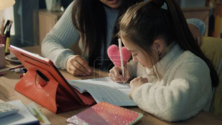 Asian family making homework, discuss new material, sitting at the table and studying together. Schoolgirl writes notes and talks with mom. Distance learning concept. Remote studying. Slow motion.