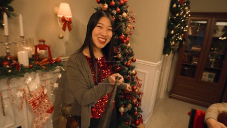 Foto de Mujer asiática con selfie stick graba vídeo para blog, muestra a su familia. Feliz familia multicultural celebrando la Navidad o Año Nuevo. Ambiente cálido de la cena familiar de Navidad en casa. Vista de cámara. - Imagen libre de derechos
