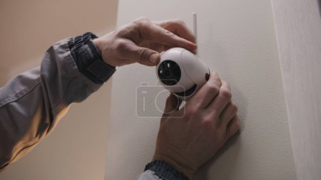 Photo for Installer in uniform puts security camera on wall fastening and connects it to system with cable. Man installs cameras in house. Concept of CCTV cameras, monitoring, safety and privacy. - Royalty Free Image