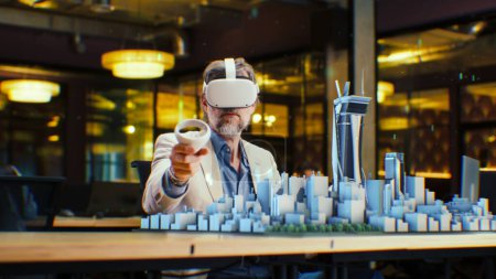 Photo for Male engineer uses VR headset and wireless controllers, creates architectural project of the city in virtual reality. Man works in modern hi-tech company. 3D hologram. Future digital AI technologies. - Royalty Free Image