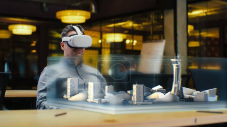 Photo for Male architect uses VR headset and wireless controllers, creates architectural project of metropolis in virtual reality. Man works in hi-tech company. 3D hologram. Future innovative AI technologies. - Royalty Free Image