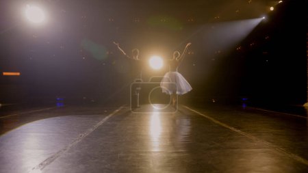 Foto de Bailarines de ballet salen de detrás de las cortinas y realizan danza en el escenario clásico del teatro iluminado por focos. Compañeros de danza practican en el ensayo de coreografía para la actuación de ballet teatral. - Imagen libre de derechos