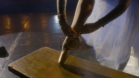Téléchargez les photos : Ballerina met des chaussures pointes pour préparer la répétition chorégraphique. Ballet danseuse commence l'entraînement et danse sur la pointe des pieds sur la scène de théâtre éclairée par des projecteurs. Ballet classique danse art. - en image libre de droit