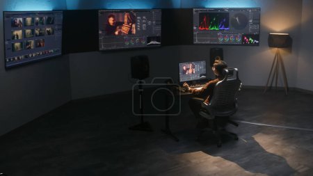 Der Video-Editor arbeitet im Studio am Computer, verwendet das Bedienfeld zur Farbkorrektur, bearbeitet Videos, macht Farbkorrekturen für Filme. Große Bildschirme mit Software-Schnittstelle mit Filmmaterial und RGB-Grafik.