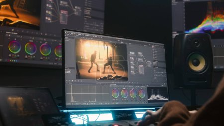 Female colorist uses color grading control panel, edits video, makes film color correction on computer in studio. Movie footage and RGB wheels on monitor. Big screens and tablet with program interface