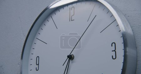Foto de Estática toma de reloj blanco con marco de metal colgando en la pared y mostrando el tiempo. Reloj de pared a pie en la oficina con diseño moderno. Reloj estricto con puntero de tiempo de ejecución rápido. De cerca.. - Imagen libre de derechos