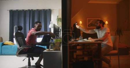 Foto de Dos hombres multirraciales se sientan frente a las computadoras en los dormitorios, hablan a través de videollamadas en línea, tienen videoconferencia. Vista de dos habitaciones o apartamentos separados por pared. Concepto de barrio y estilo de vida. - Imagen libre de derechos