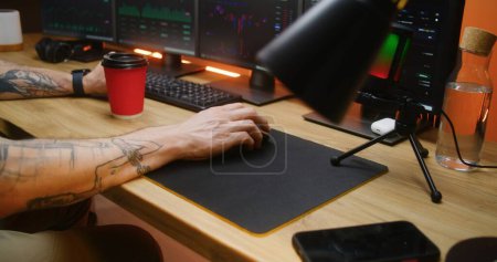 Photo for Male trader uses computer mouse, types on keyboard, analyzes real-time stocks, exchange market charts on multi-monitor PC. Man works remotely in investment or cryptocurrency at home office. Close up. - Royalty Free Image