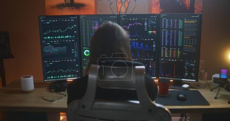 Photo for Back view of male stock trader watching real-time stocks, exchange market charts on multi-monitor computer workstation, drinking coffee. Man works in investment at home office. Cryptocurrency trading. - Royalty Free Image