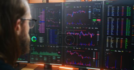 Photo for Focused trader, analyst looks at computer screen with multiple monitors, analyzes real-time stocks, exchange market charts. Man works remotely in investment at home office. Cryptocurrency trading. - Royalty Free Image