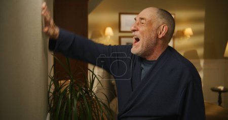 Photo for Elderly man irritated by noisy neighbor, screams, knocks on wall. Low level of sound insulation. - Royalty Free Image