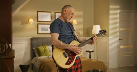 Elderly man sings and plays on electric guitar at home.