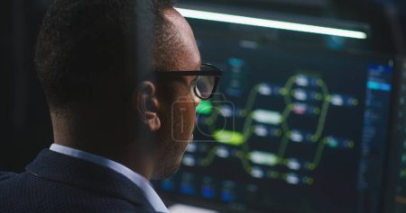 Photo for African American software engineer looks at computer screen with displayed big data server and blockchain network, monitors real-time analysis charts in monitoring office. Concept of cyber security. - Royalty Free Image