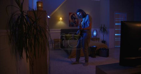 Foto de Hombre toca la guitarra eléctrica por la noche en el apartamento con luces parpadeantes. Concepto de música, entretenimiento. - Imagen libre de derechos
