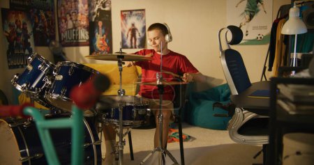 Foto de Niño en auriculares practica habilidades de músico usando kit de batería en casa. - Imagen libre de derechos