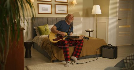 Photo for Elderly man sings and plays on electric guitar at home. - Royalty Free Image
