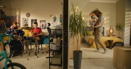 Photo for Man plays guitar in bedroom. Young boy plays drum kit and young girl plays ukulele, jumps on bed. View of two rooms or apartments separated by wall. Concept of music, neighbourhood and lifestyle. - Royalty Free Image