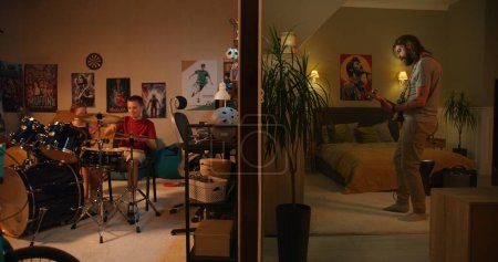 Photo for Man plays guitar in bedroom. Young boy and girl living next door, playing drum kit and ukulele at home in the evening. View of two rooms or apartments separated by wall. Concept of neighbourhood. - Royalty Free Image