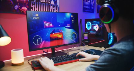 Photo for Young gamer plays in car racing simulator on PC at home. Computer monitor with displayed online video game live stream or cybersport championship. Desk illuminated by RGB LED strip light. - Royalty Free Image