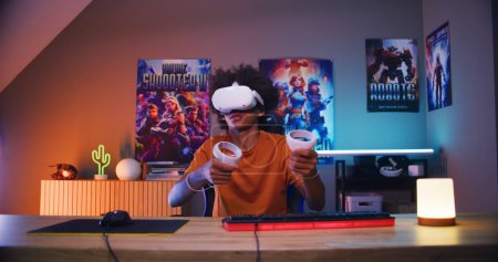 Photo for Teenage gamer in VR headset plays virtual online video game using wireless controllers. African American guy having fun in leisure time in his room. Gaming at home. View from PC screen perspective. - Royalty Free Image