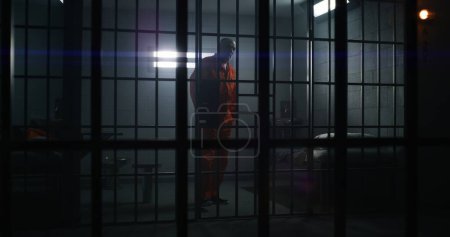 Foto de Dos reclusos culpables en un centro de detención o correccional. Un anciano criminal con uniforme naranja se sienta en la cama de la cárcel y habla con su compañero de celda. Presos sombríos cumplen condena de prisión en celda de prisión. - Imagen libre de derechos