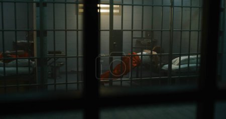 Foto de Una prisionera con uniforme naranja yace en la cama, y otra boxea en la celda de la prisión. Las mujeres reclusas cumplen penas de prisión por crímenes en la cárcel. Criminales en un centro de detención o correccional. - Imagen libre de derechos