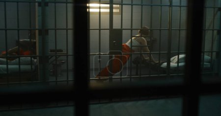 Foto de Una prisionera con uniforme naranja yace en la cama, y otra boxea en la celda de la prisión. Las mujeres reclusas cumplen penas de prisión por crímenes en la cárcel. Criminales en un centro de detención o correccional. - Imagen libre de derechos