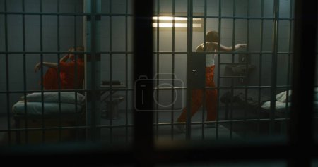 Photo for One female prisoner in orange uniform lies on the bed, another boxing in prison cell. Women inmates serve imprisonment terms for crimes in jail. Criminals in detention center or correctional facility. - Royalty Free Image